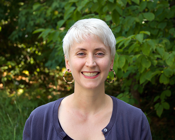 A woman in a purple shirt in front of a nature background.