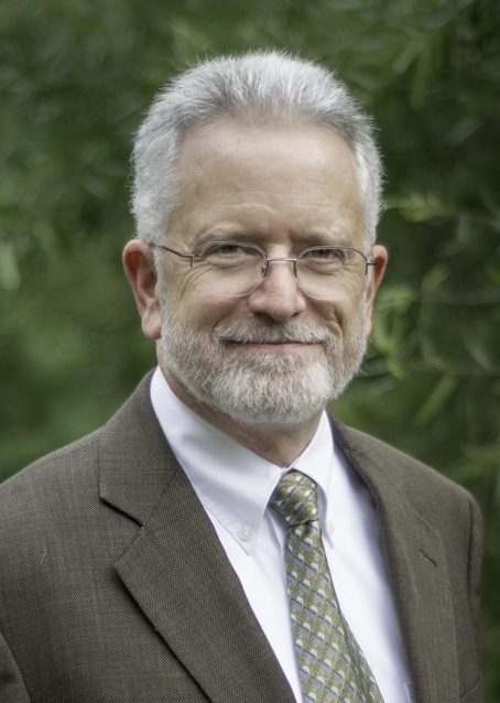 Man in light brown suit with glasses in a nature background.