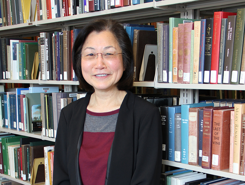 A woman in glasses standing in front of book shelves.