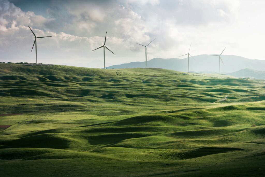 Foreground of green rolling hills with wind turbines in the background.